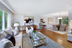 Living and dining area with oversized windows overlooking greenery, hardwood floors, and contemporary furnishings.