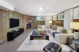 Finished lower-level family room with gas fireplace, wood panel walls, and sectional sofa at 12 Vistaview Blvd.