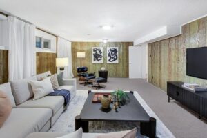 Finished lower-level family room with gas fireplace, wood panel walls, and sectional sofa at 12 Vistaview Blvd.