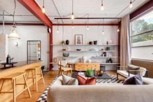 Beige couch in the foreground facing a wall of built-in shelving. Industrial style lighting hangs from the ceiling.
