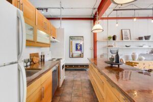 Galley style kitchen with wall of cabinets, sink, and dishwasher on the left side. Prep island with built-in storage on the right side.