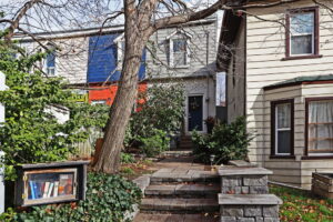 Two-storey home at 21 Blackburn St in Toronto, framed by mature trees and greenery, with a stone walkway leading up to a dark front door.