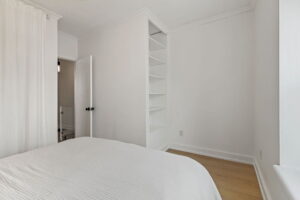 Second-floor bedroom at 21 Blackburn St with built-in shelving, white walls, wood floors, and a doorway leading to the the hall.