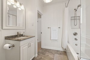 Spacious bathroom at 21 Blackburn St with a granite-topped vanity, white panelled walls, tiled floors, and a combined tub and shower with glass panel and modern fixtures.