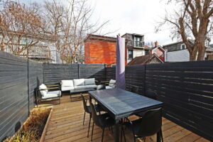 Fenced backyard deck at 21 Blackburn St with outdoor dining table, seating area, and black privacy fencing, surrounded by neighbouring homes and mature trees.