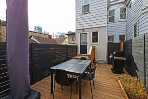 Rear deck at 21 Blackburn St with outdoor dining area, barbecue, planter boxes, and black privacy fencing, leading to the back entry of the home.